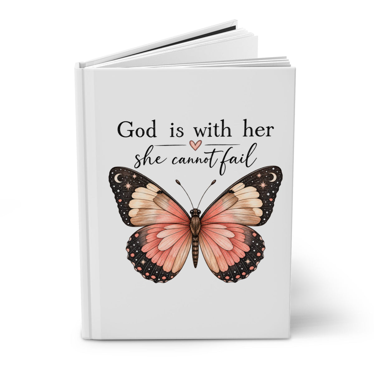 A white hardcover journal or notebook standing upright on a white background, featuring the printed quote 'God is with her she cannot fail' in black script with a small pink heart, and a large pink and black butterfly illustration on the front.