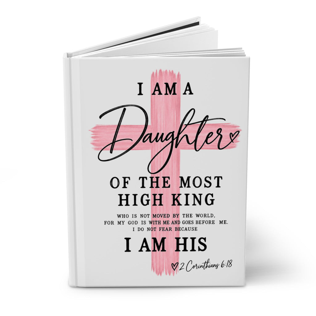 A hardcover book with a white cover featuring a pink painted cross and black text that reads, 'I AM A Daughter OF THE MOST HIGH KING' and 'I AM HIS' with a Bible verse below, shown on a white background.